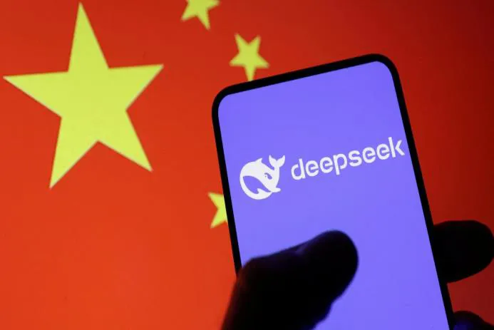 A hand holding a smartphone displaying the DeepSeek logo against the backdrop of the Chinese flag.