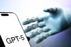 A close-up of a smartphone displaying 'GPT-5' with a robotic hand reaching towards it, symbolizing advancements in AI technology.