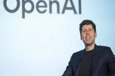 Speaker at an OpenAI event presenting with a smile against a backdrop featuring the OpenAI logo.